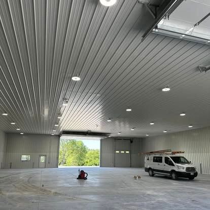 Interior of a large industrial building with a van and open door; concrete floor, metal ceiling, and walls.