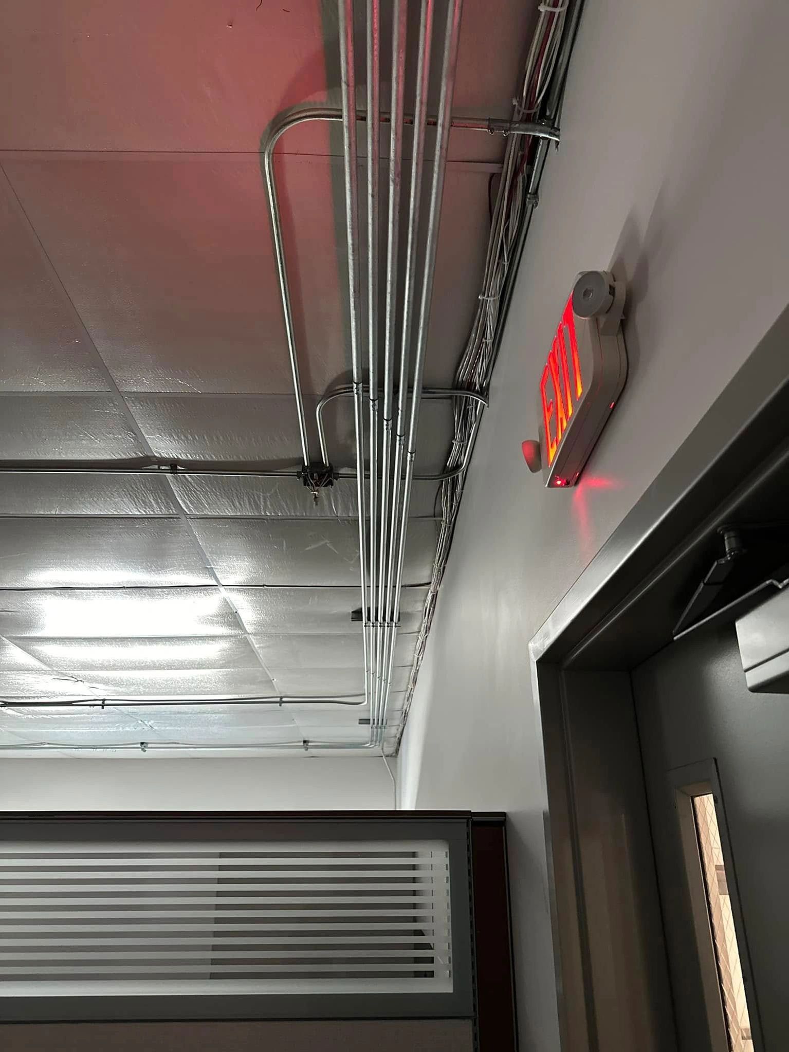 Red exit sign above doorway, electrical conduit on wall and ceiling.