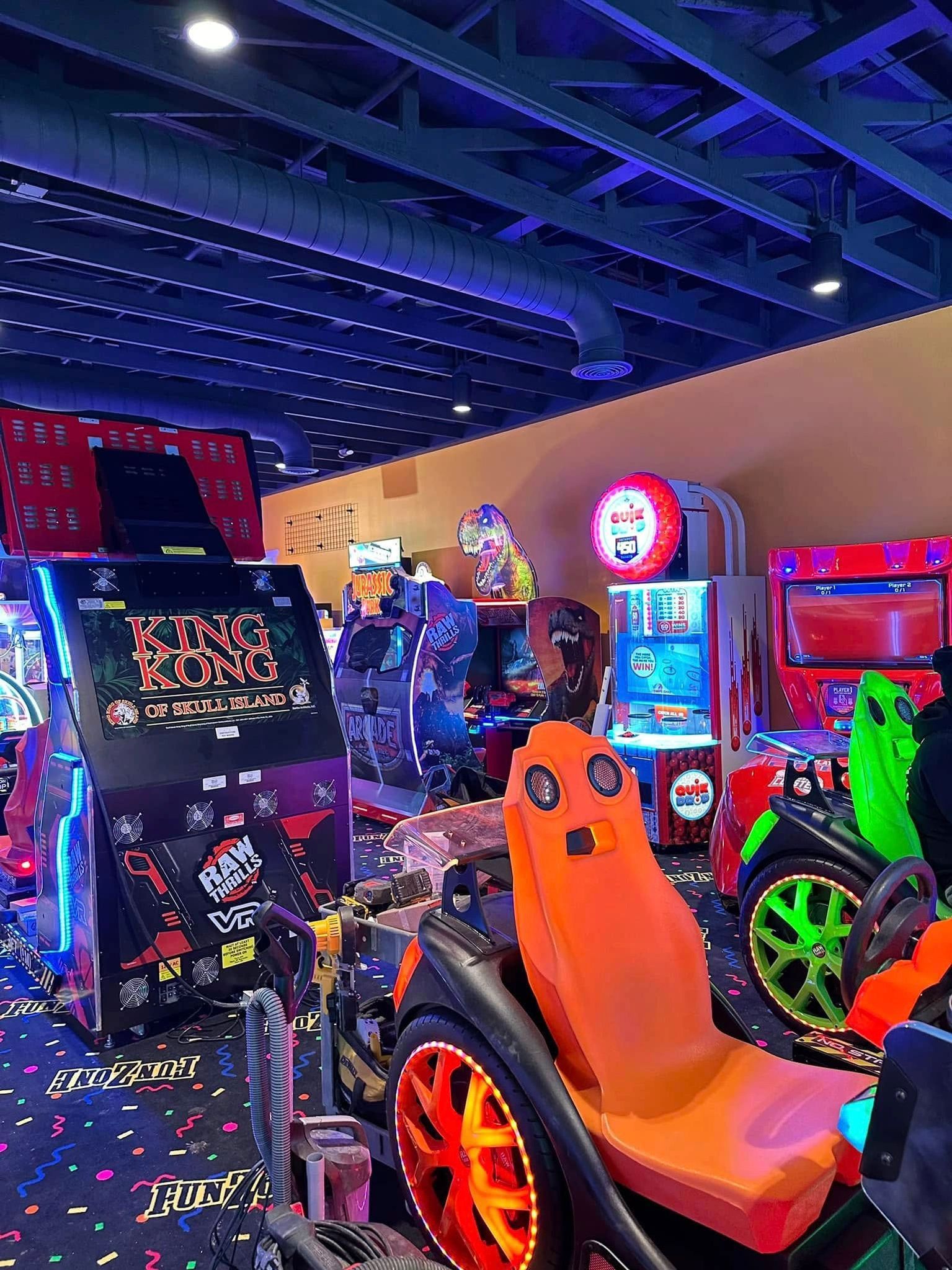 Arcade with racing game, other game machines, orange seat, neon lights, patterned carpet.