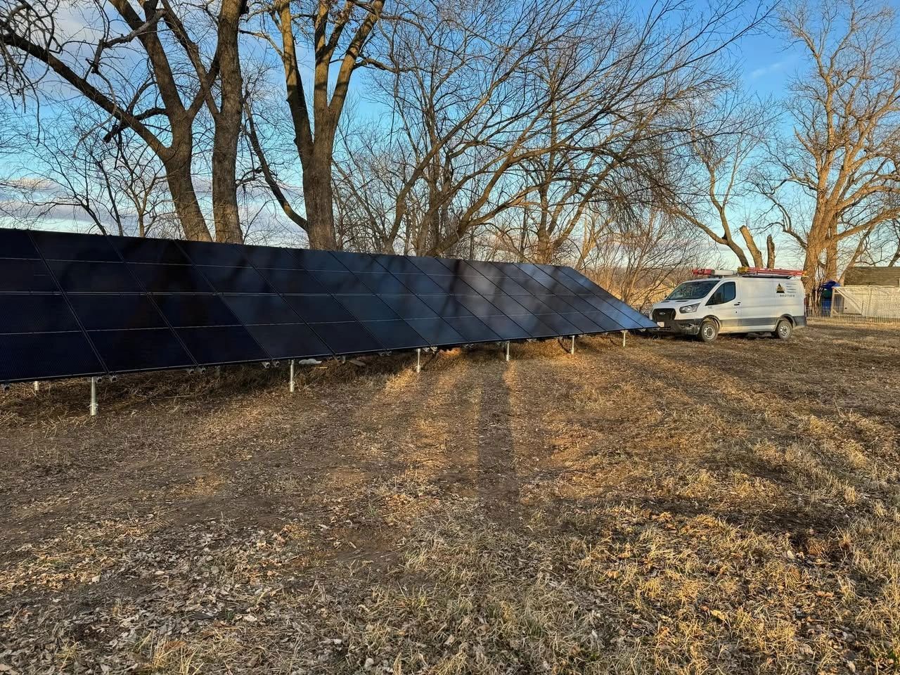 Solar panel array in a field with service van parked nearby, under a blue sky and bare trees.