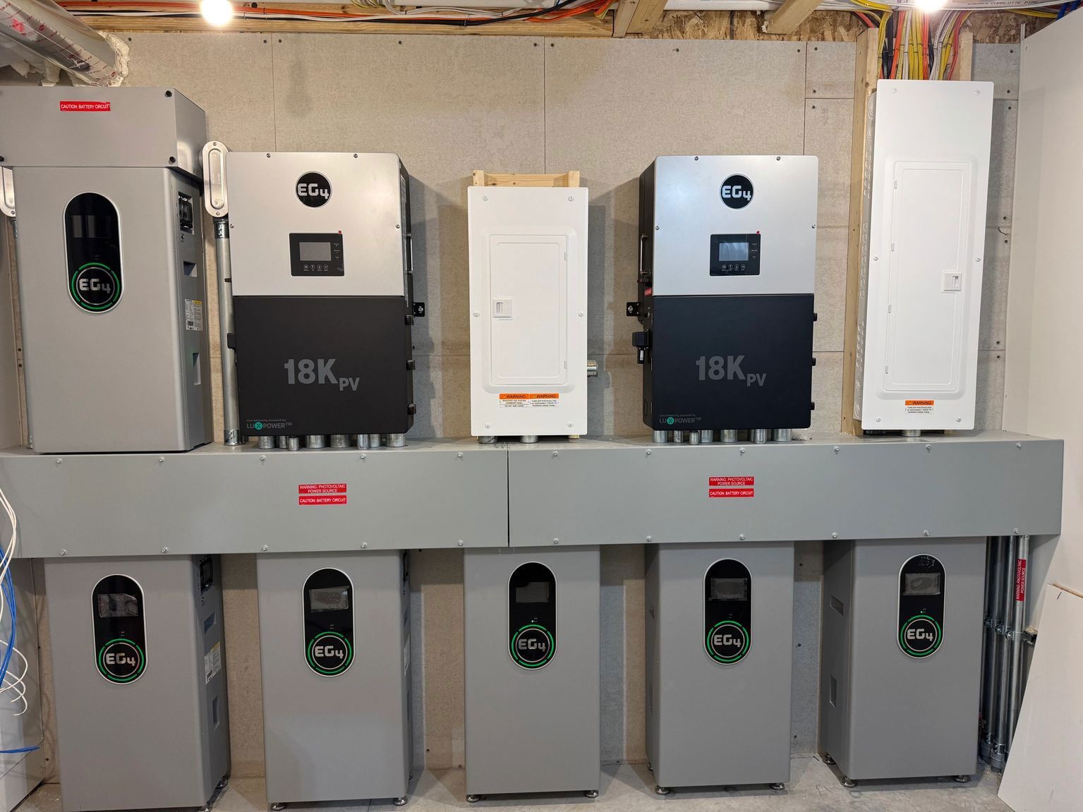 Solar inverters mounted on a wall in a basement, gray and black units.