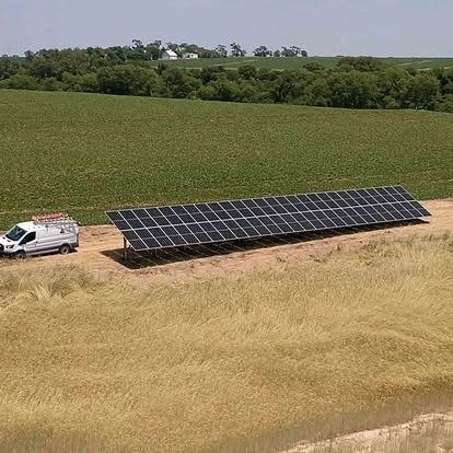 Solar panel array beside a van on a dirt road, adjacent to a field.