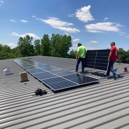 Two workers install solar panels on a metal roof under a blue sky.