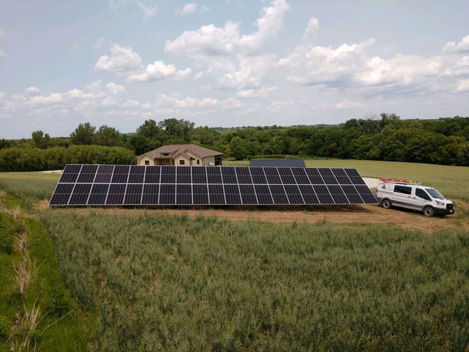 Solar panel array in a field with a house in the background and a service van.