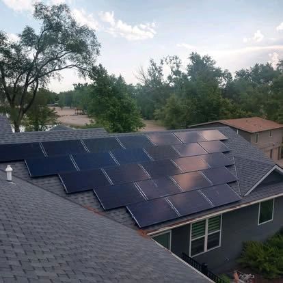 Solar panels on a residential roof, trees in the background, cloudy sky.