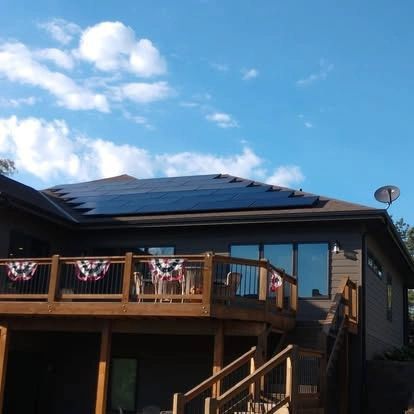 House with solar panels on roof, deck with patriotic bunting, and satellite dish against a blue sky.