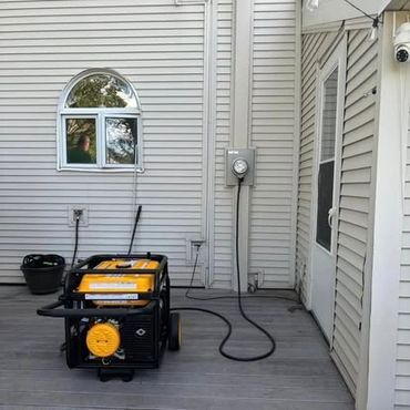 A portable generator is connected to a house via a transfer switch on a deck.