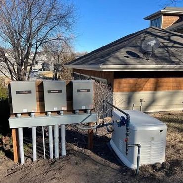 Solar panel inverters and a generator beside a house on a sunny day.