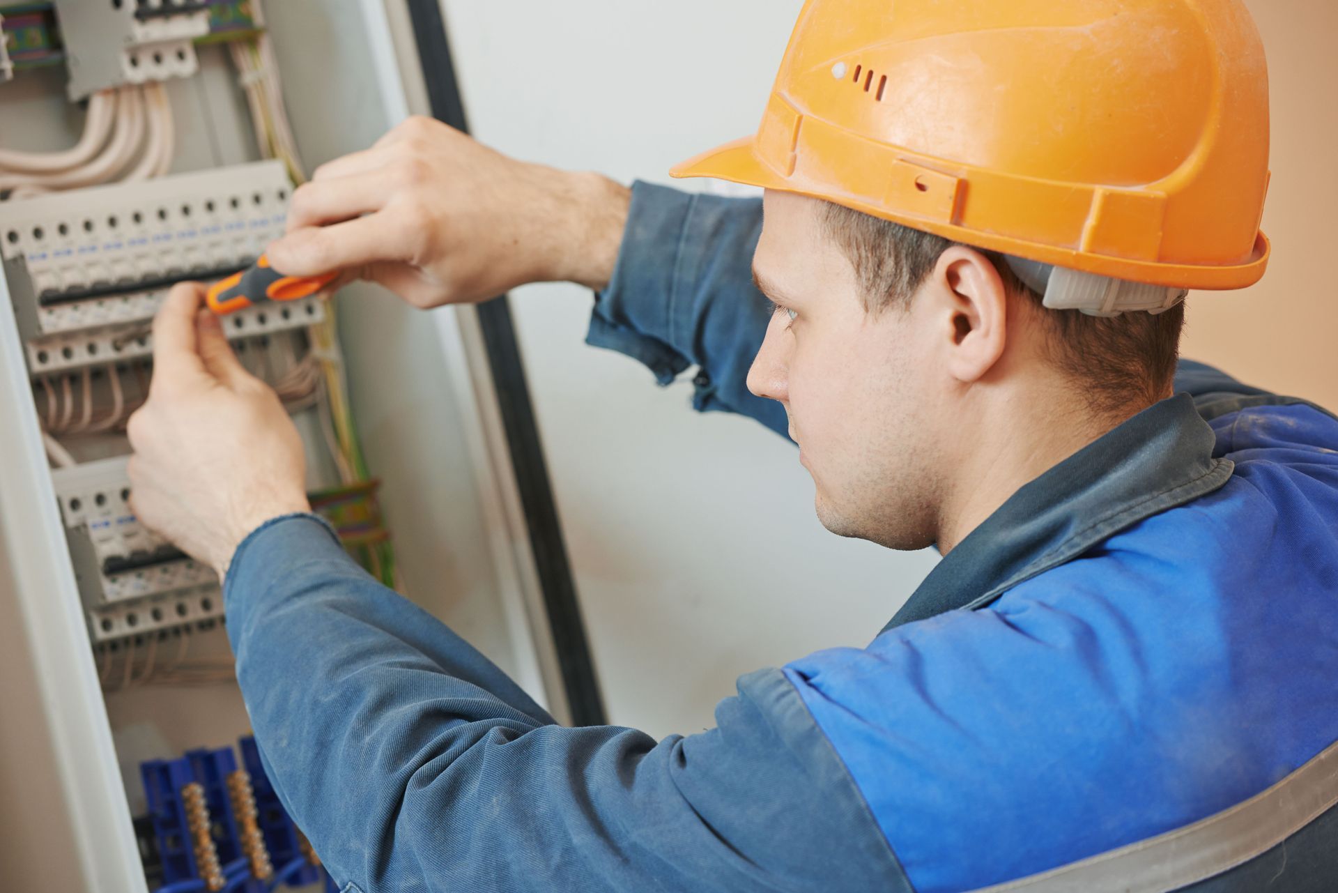 A man wearing a hard hat is working on an electrical box.