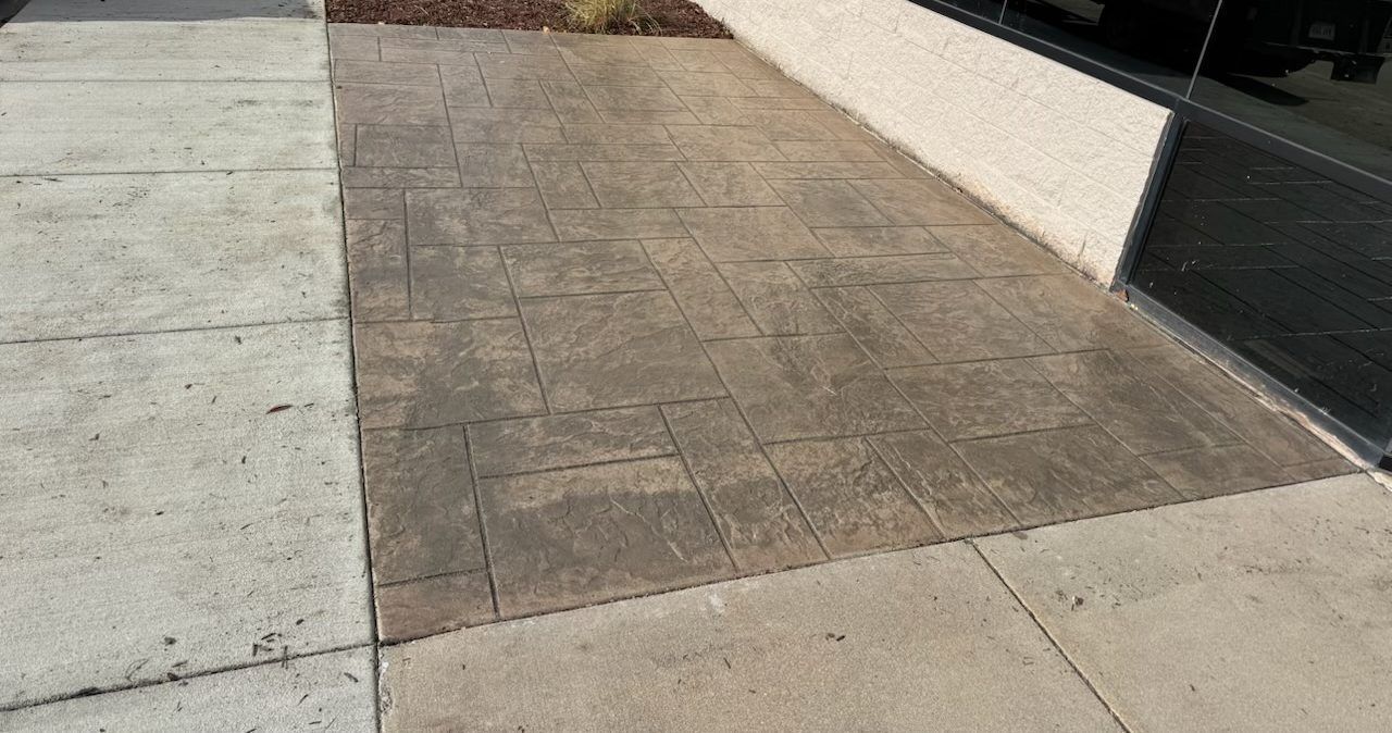 Concrete sidewalk with a darker stamped section beside a white wall and curb.