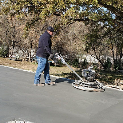 Worker using a power trowel to smooth fresh concrete on a driveway outdoors