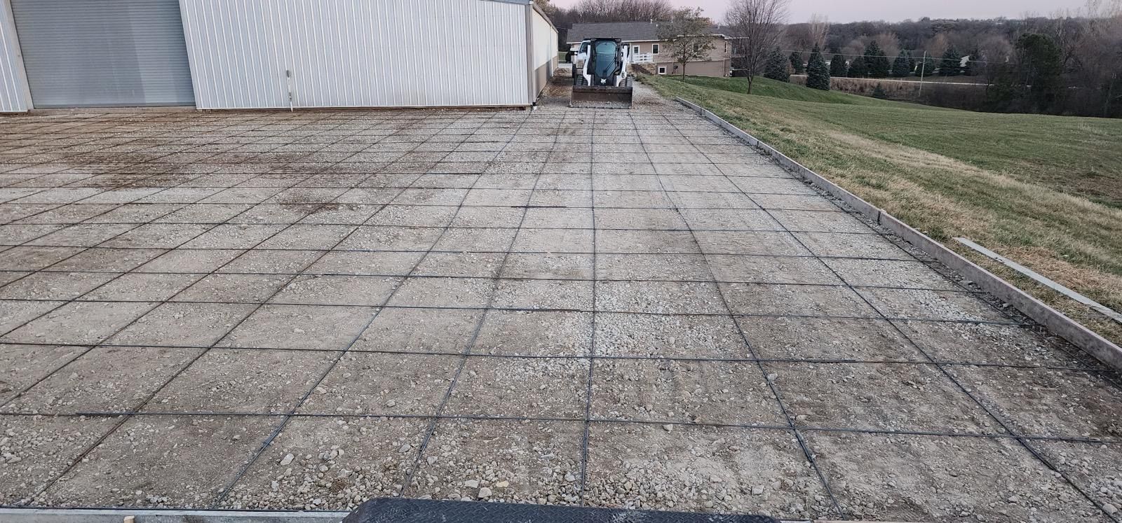 Long paved driveway beside a building, leading to a distant vehicle under an overcast sky.