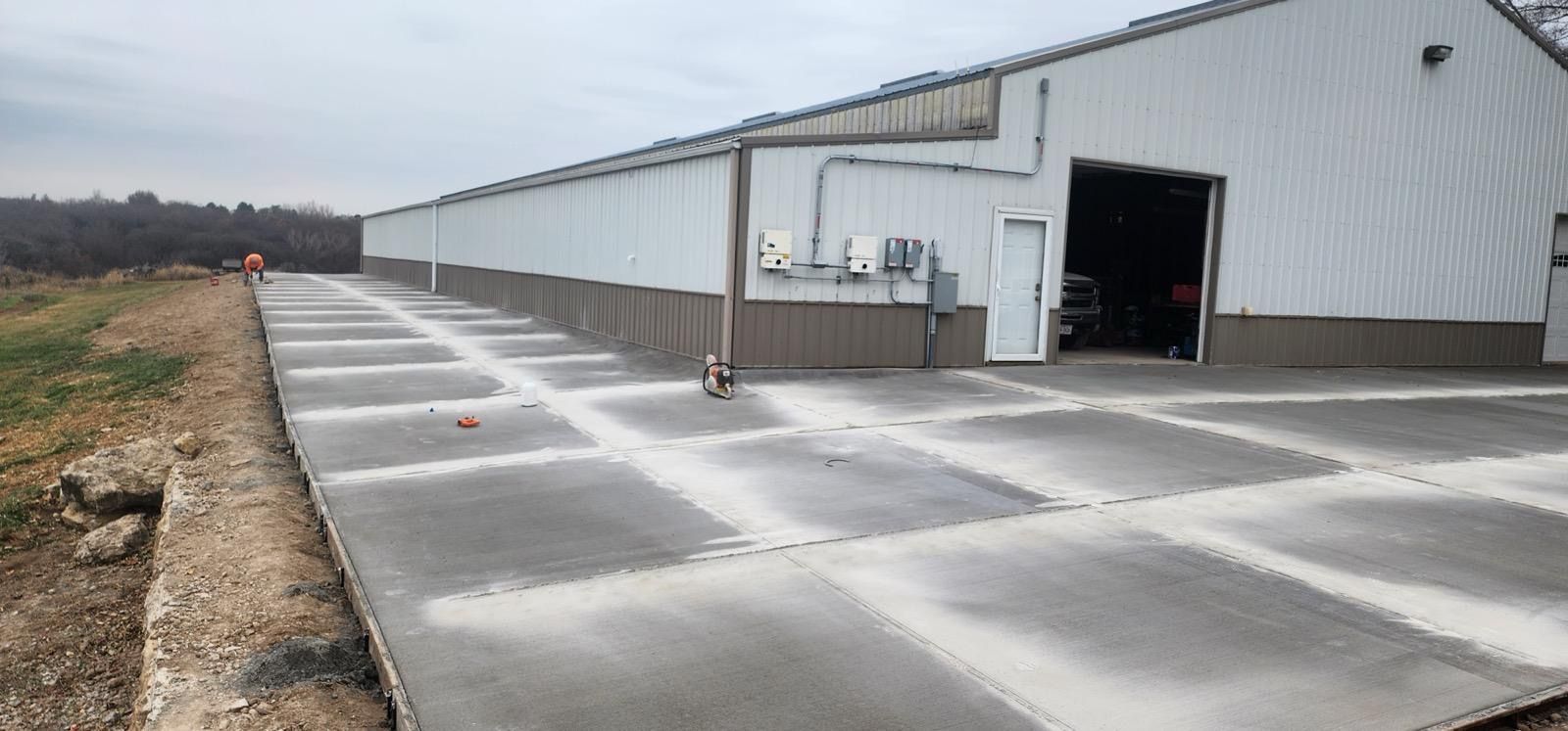 Long white industrial building with a concrete apron and open garage door on an overcast day