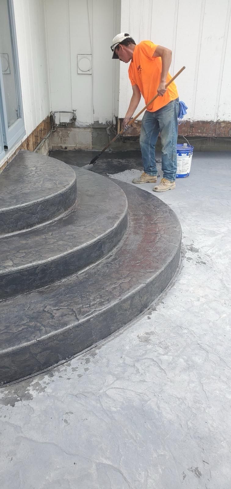 Worker in orange shirt painting the exterior edge of a curved concrete staircase.