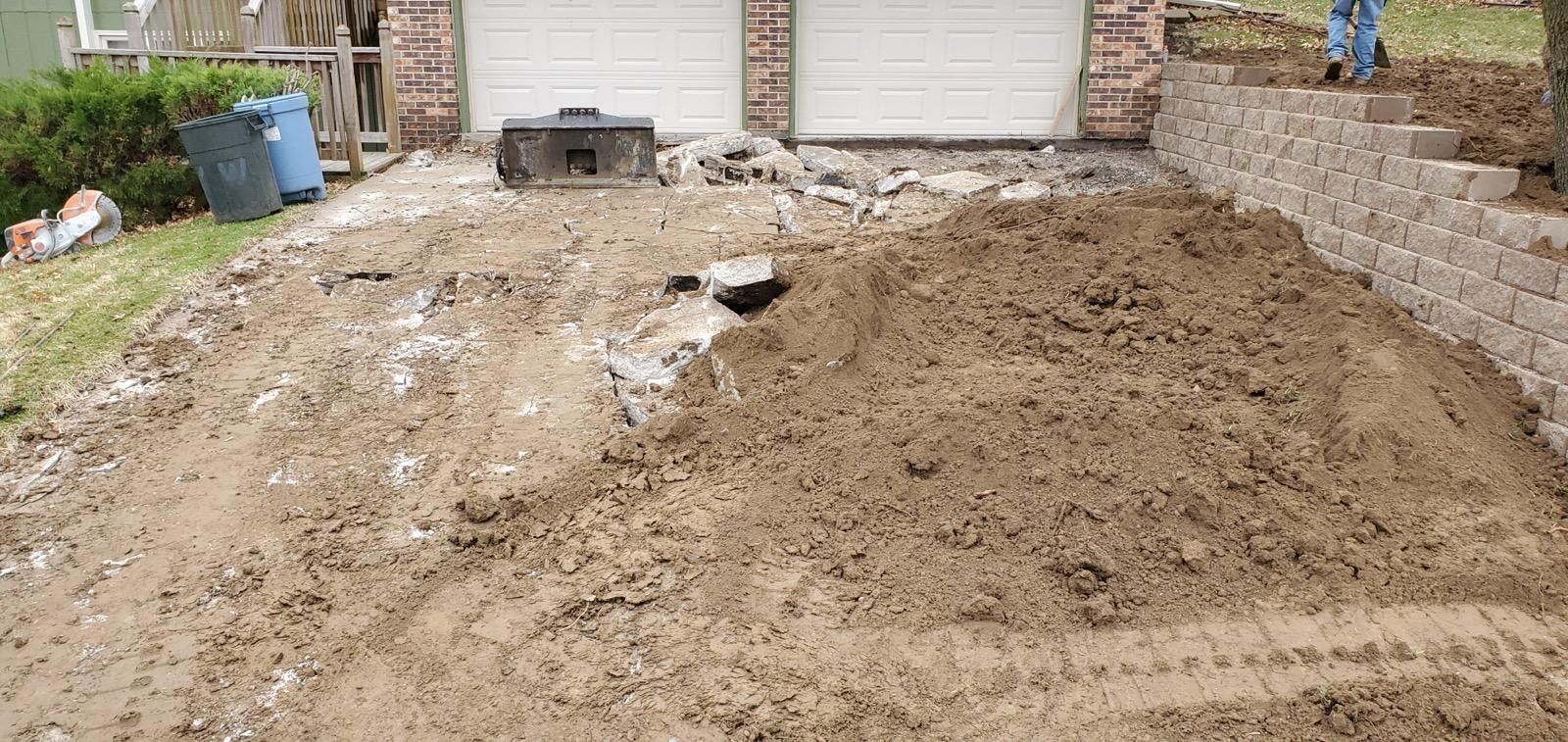 Freshly graded dirt lot beside a driveway, with retaining wall and garage doors in the background
