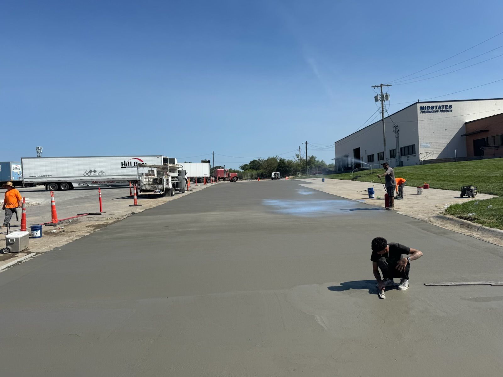 Roadwork crew smoothing wet concrete on a street beside industrial buildings