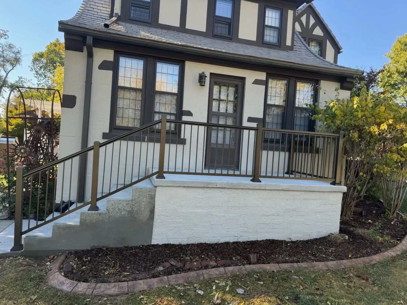 Front entry of a house with black railings, white steps, and dark trim under a steep roof.