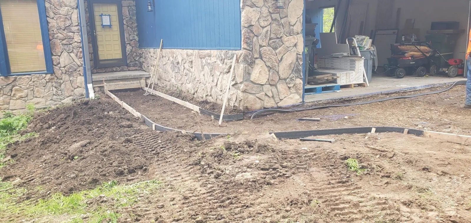Stone house exterior with muddy yard, blue doors, and a garage-like opening