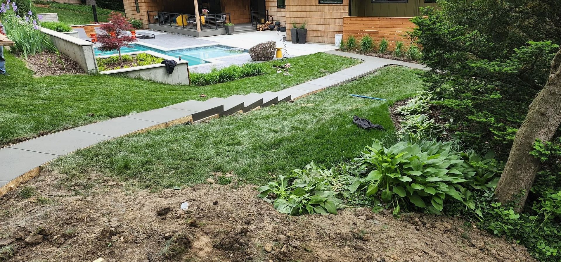 Gravel path through a lush garden toward a house, with a blue pool and greenery beside it