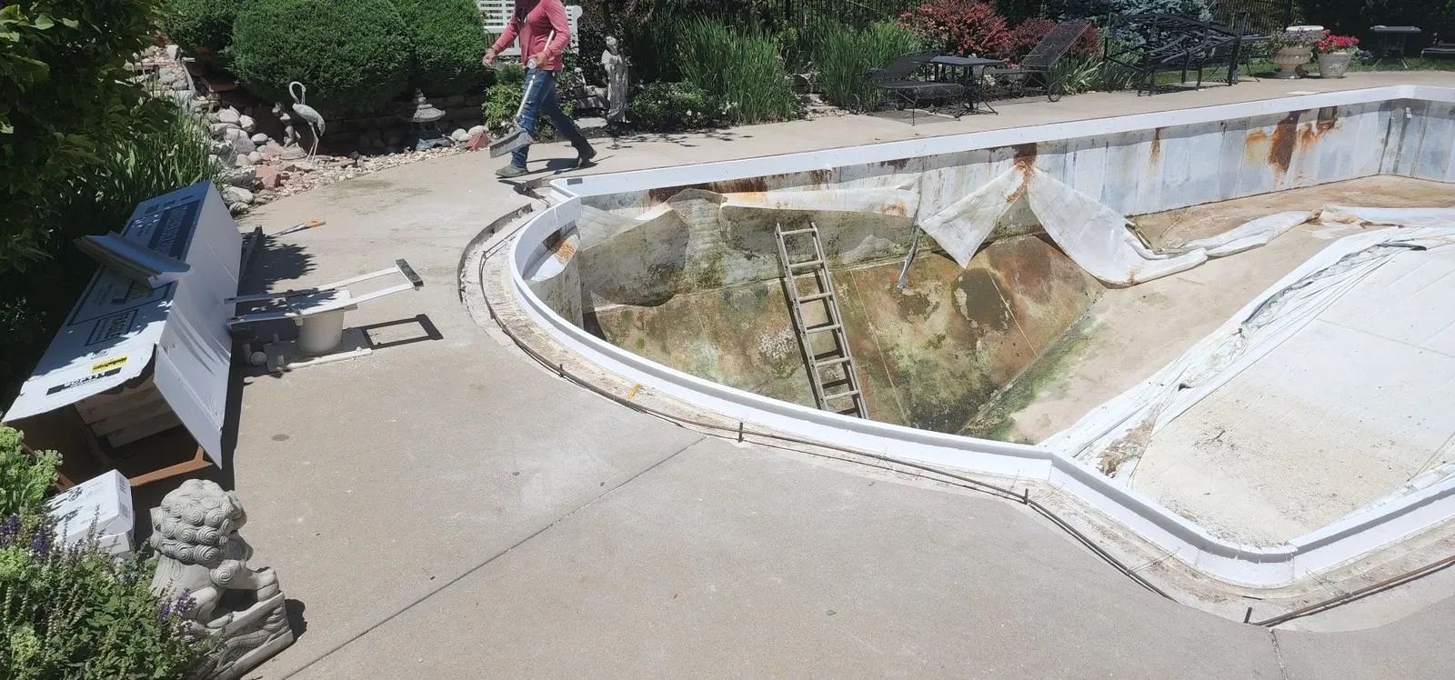 Empty outdoor pool with cracked concrete; a person in a pink shirt walks nearby.