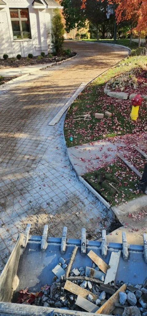 Curved brick walkway beside a landscaped flower bed, with construction debris in the foreground.