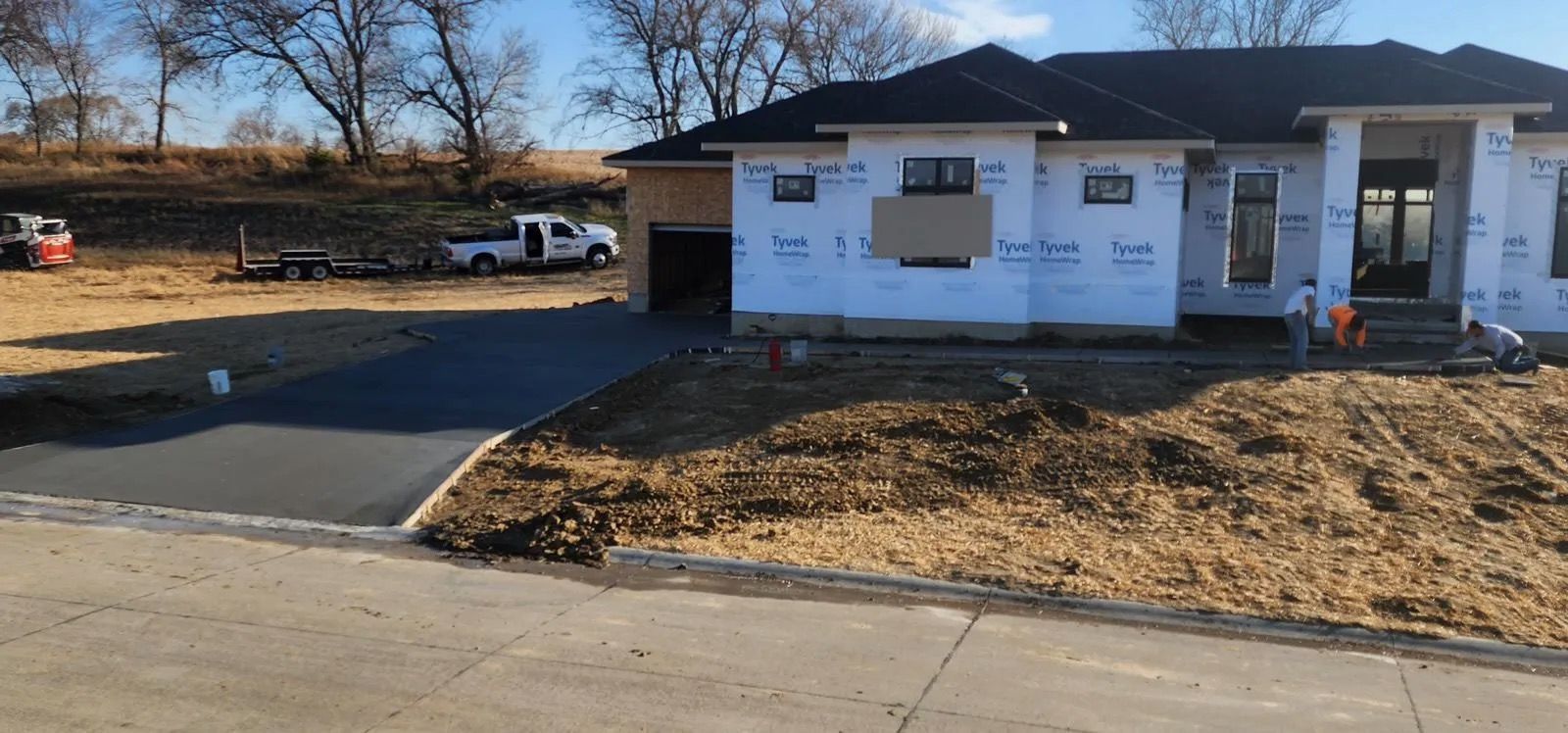 Partially built white house with driveway and bare dirt front yard on a sunny day