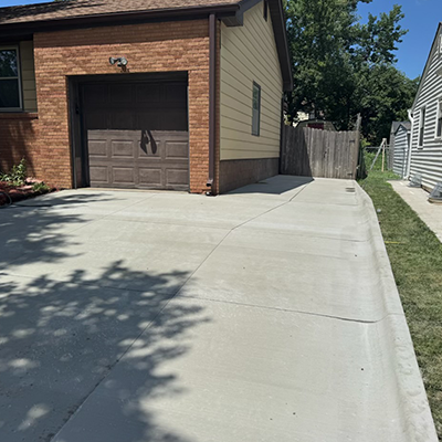 Driveway beside a brick garage with a concrete pad and wooden fence on a sunny day