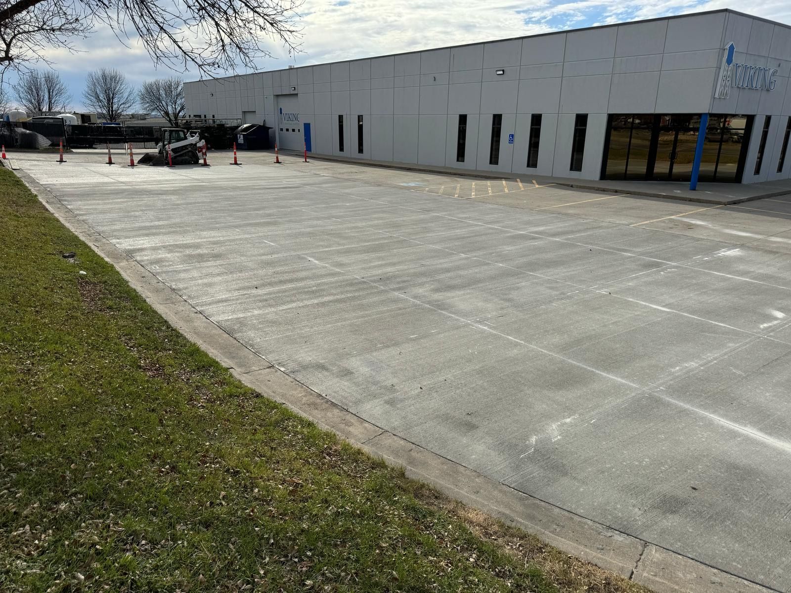 Empty parking lot beside a light-gray commercial building on a cloudy day.