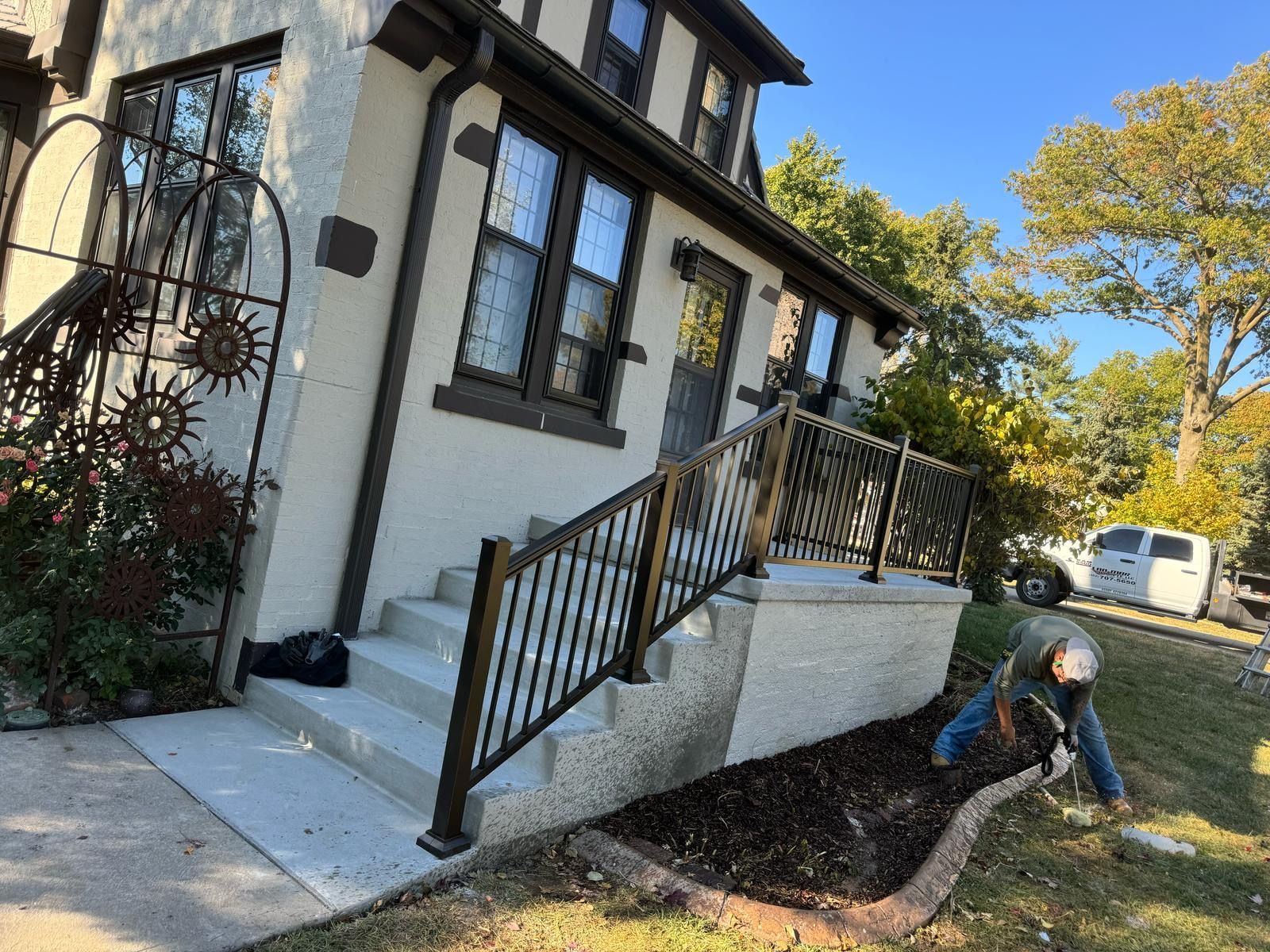Front steps of a white house with black railing, a ramp, and a worker clearing soil near the foundation.