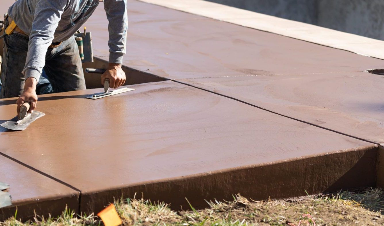 Worker smoothing a large brown concrete slab outdoors with a trowel