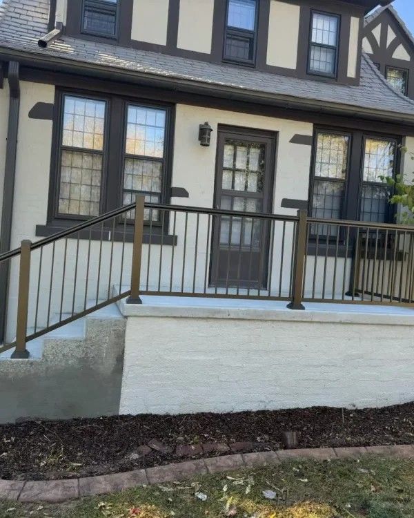 Front porch of a house with dark trim, railing, and steps leading to a front door.
