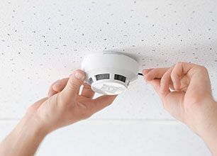 A person is installing a smoke detector on the ceiling.