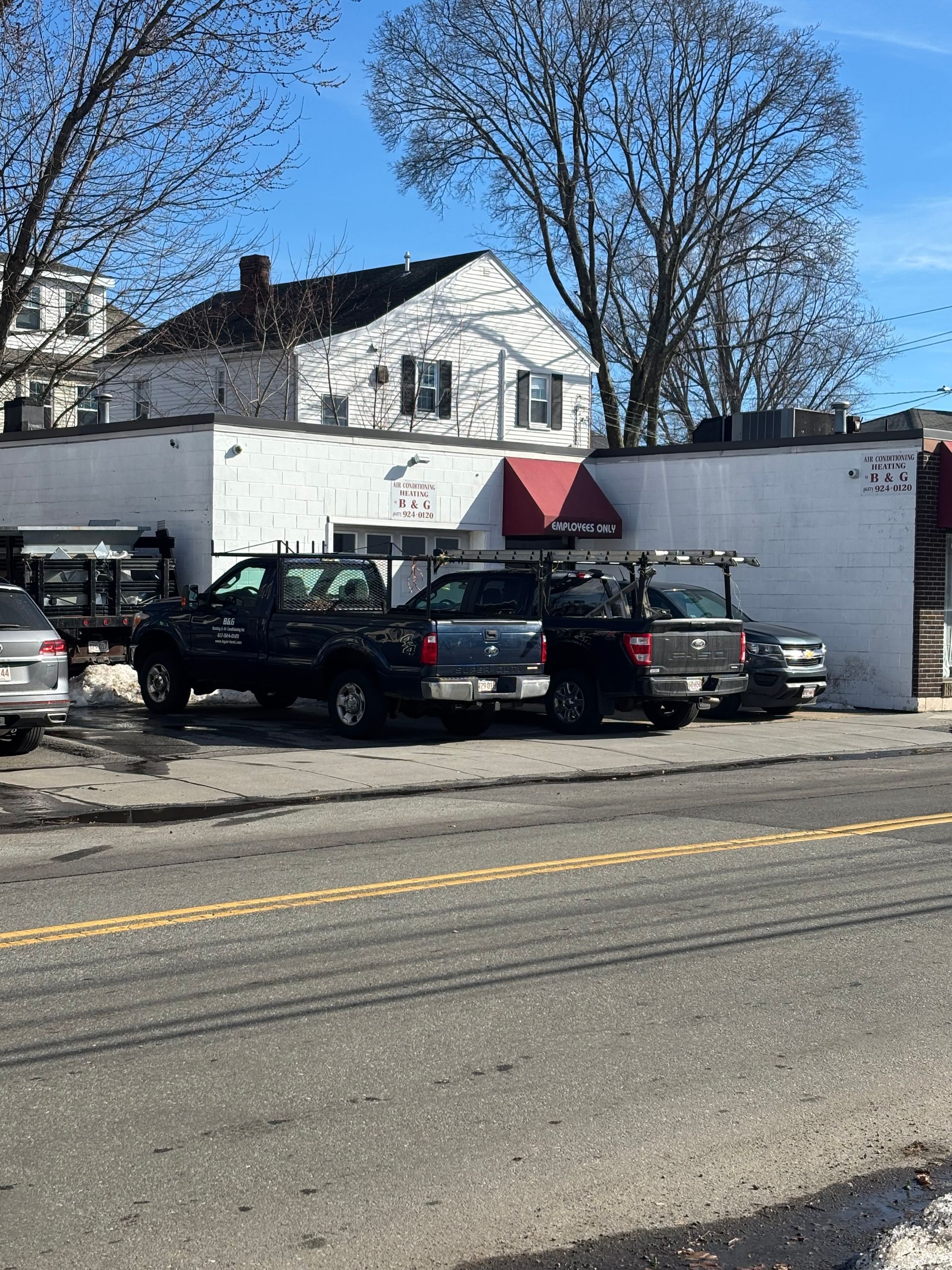 A white building with a red awning and black pickup trucks parked in front, under a clear blue sky.