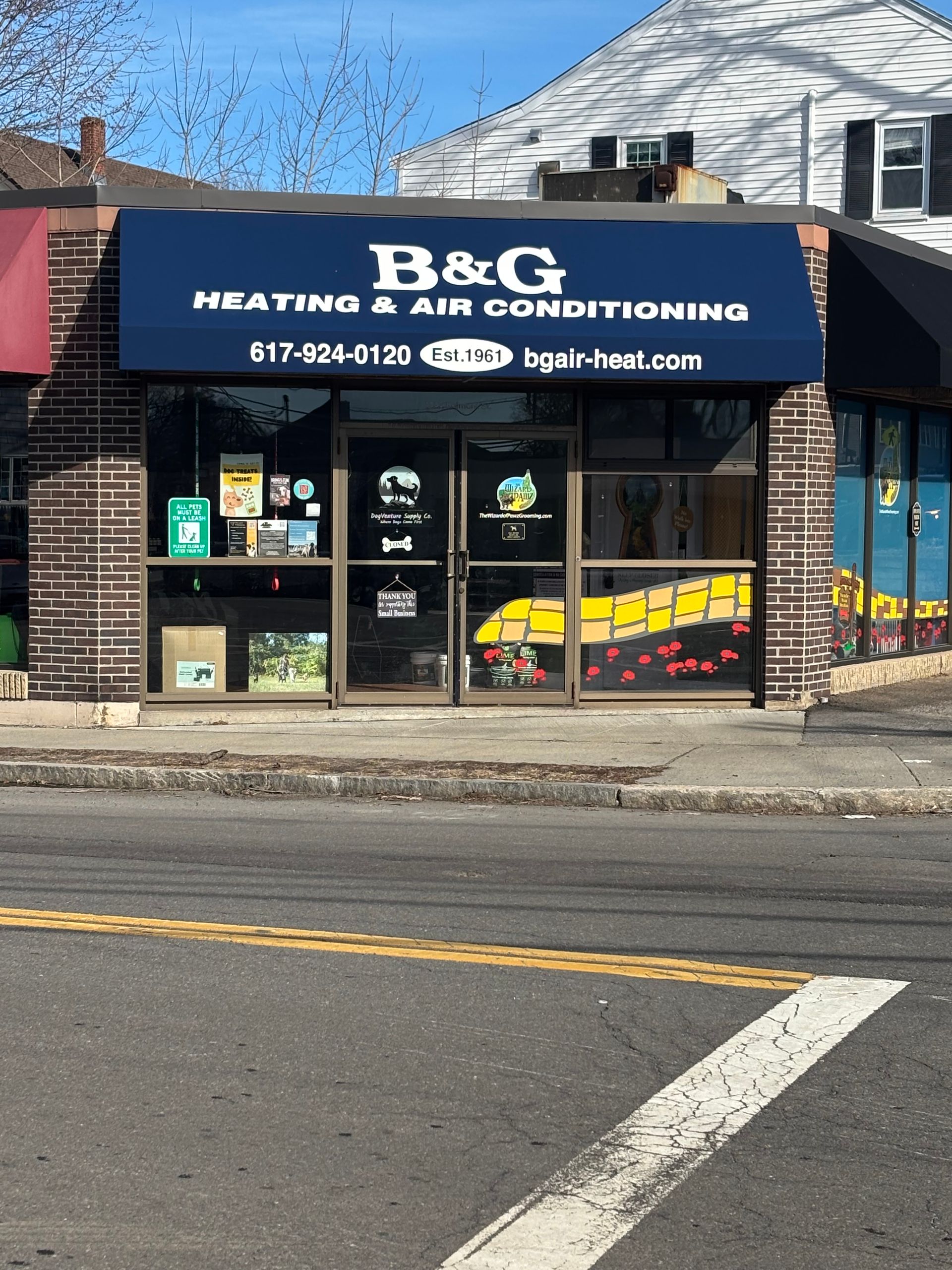 Storefront for B&G Heating & Air Conditioning with a blue awning, brick exterior, and glass doors on a sunny day.