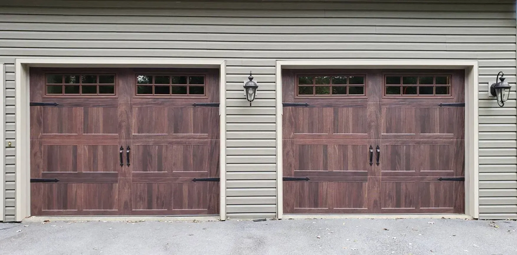 Two wooden garage doors on a beige house exterior with a wall lantern between them.