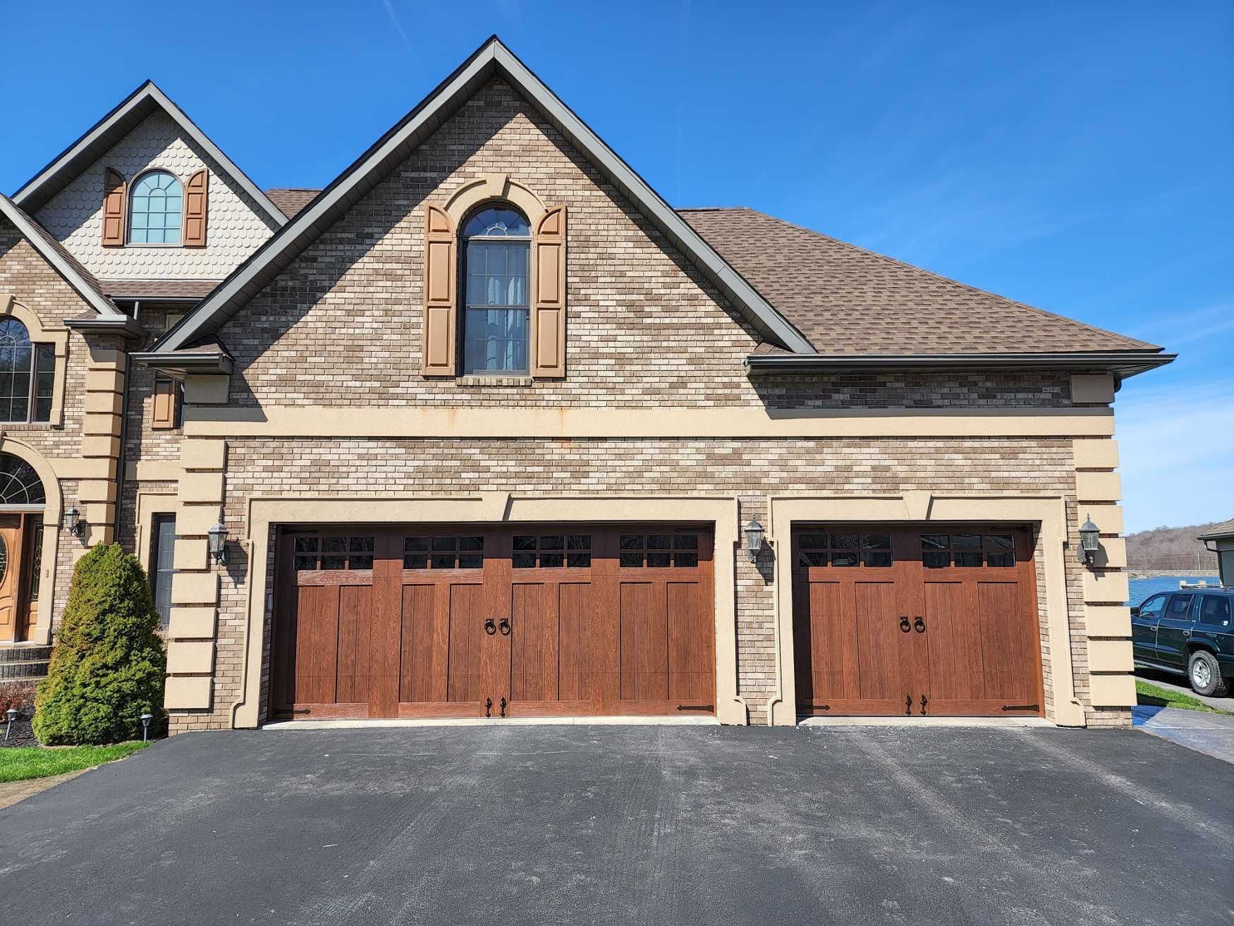 Stone suburban house with three brown garage doors and a paved driveway