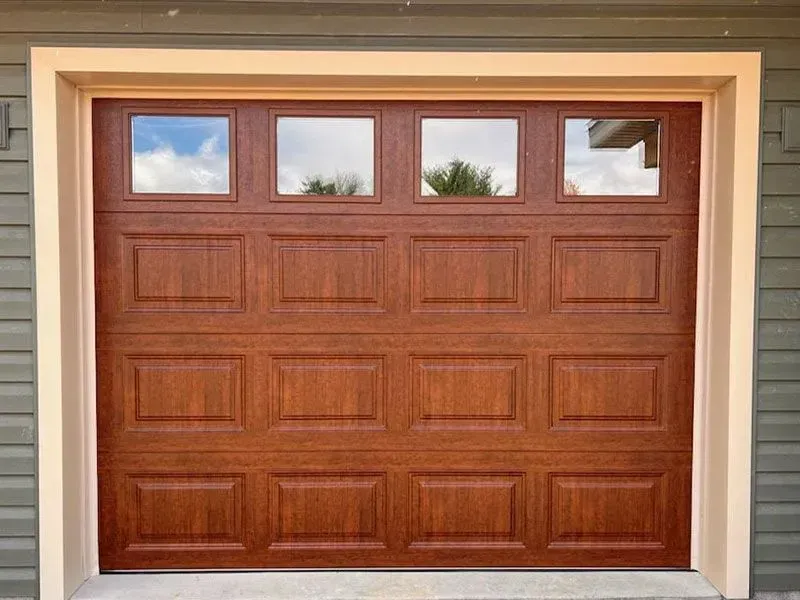 Closed brown wooden garage door with four small windows at the top, framed by beige trim.