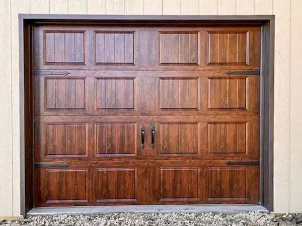 Brown wooden double garage door with rectangular panels and dark handles, set in a stucco wall