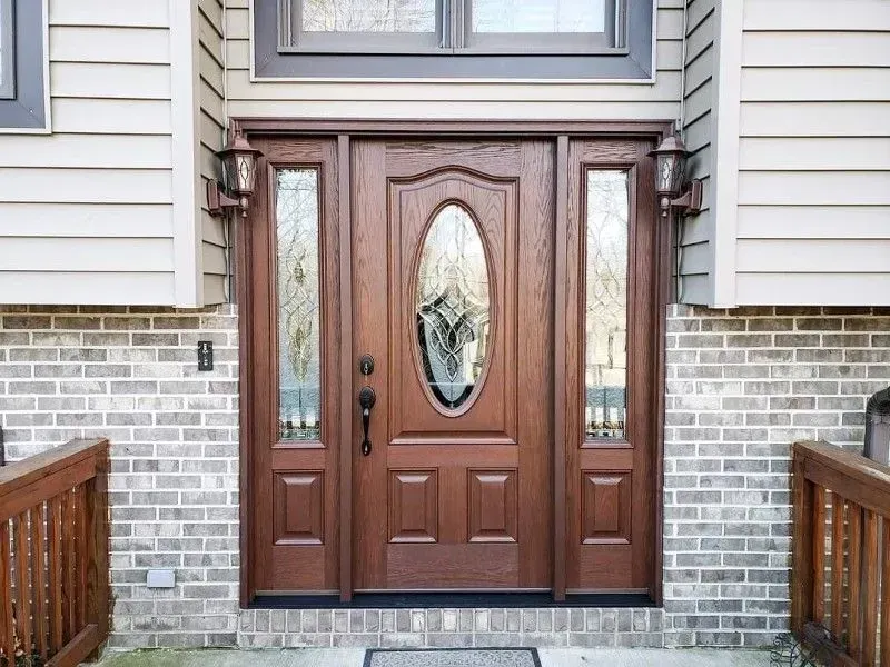 Front door with oval glass insert, flanked by sidelights, set in a brick and siding entryway.