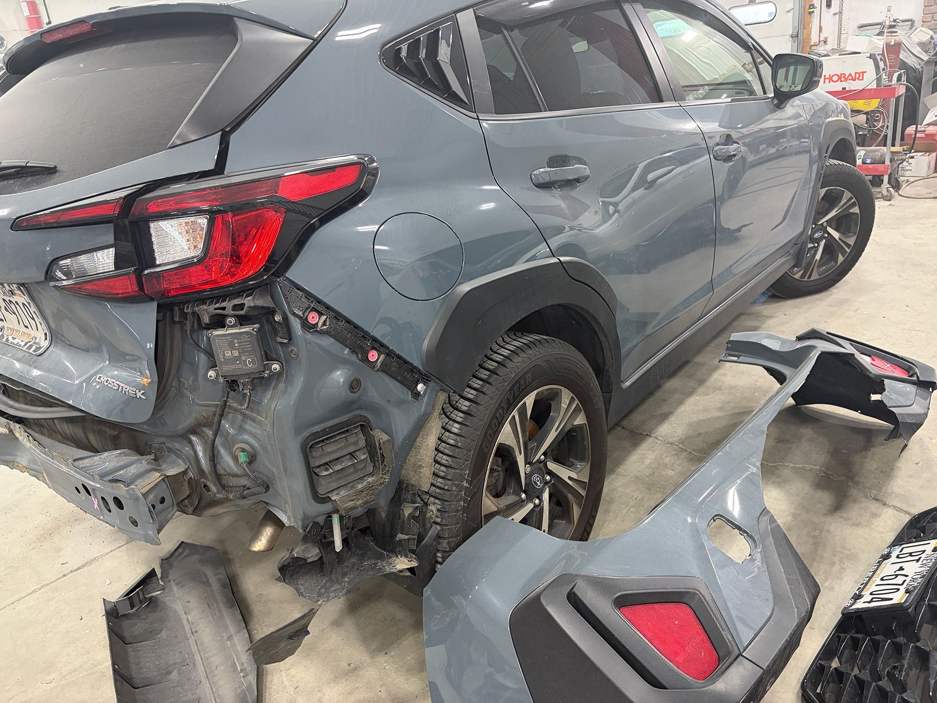 Damaged gray SUV with rear-end collision damage in a repair shop, detached bumper in foreground