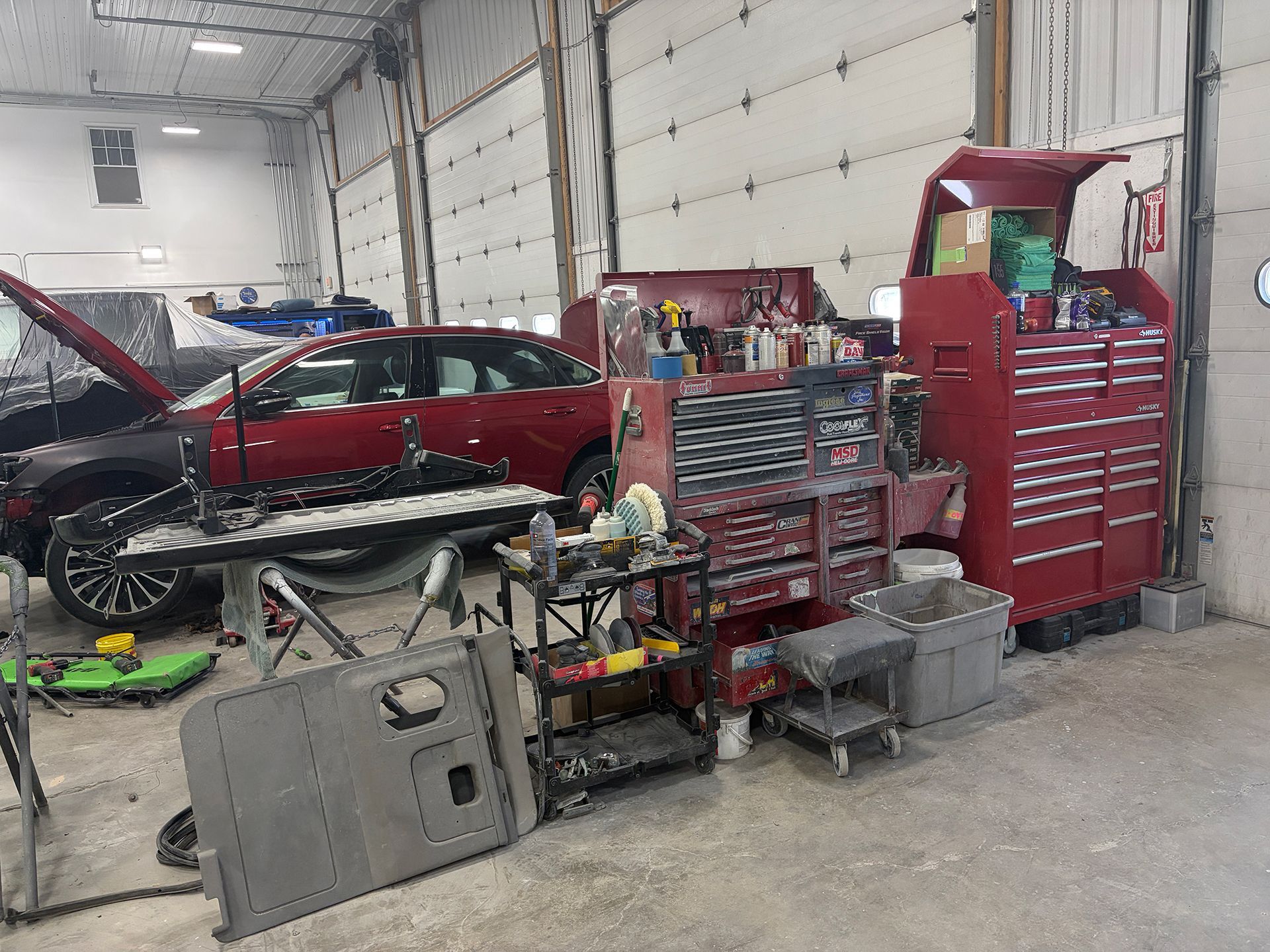 Auto repair shop with red car, tool cabinets, and scattered equipment in a garage
