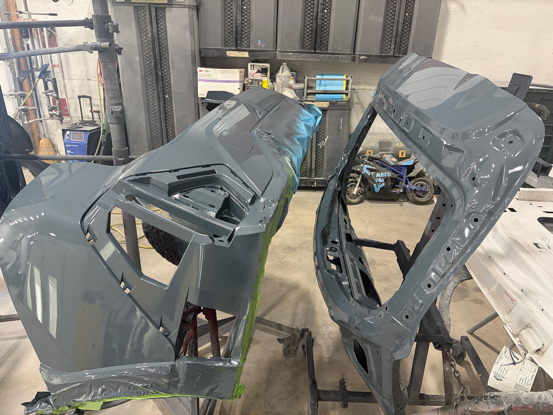 Two gray car body panels hanging in an auto body shop