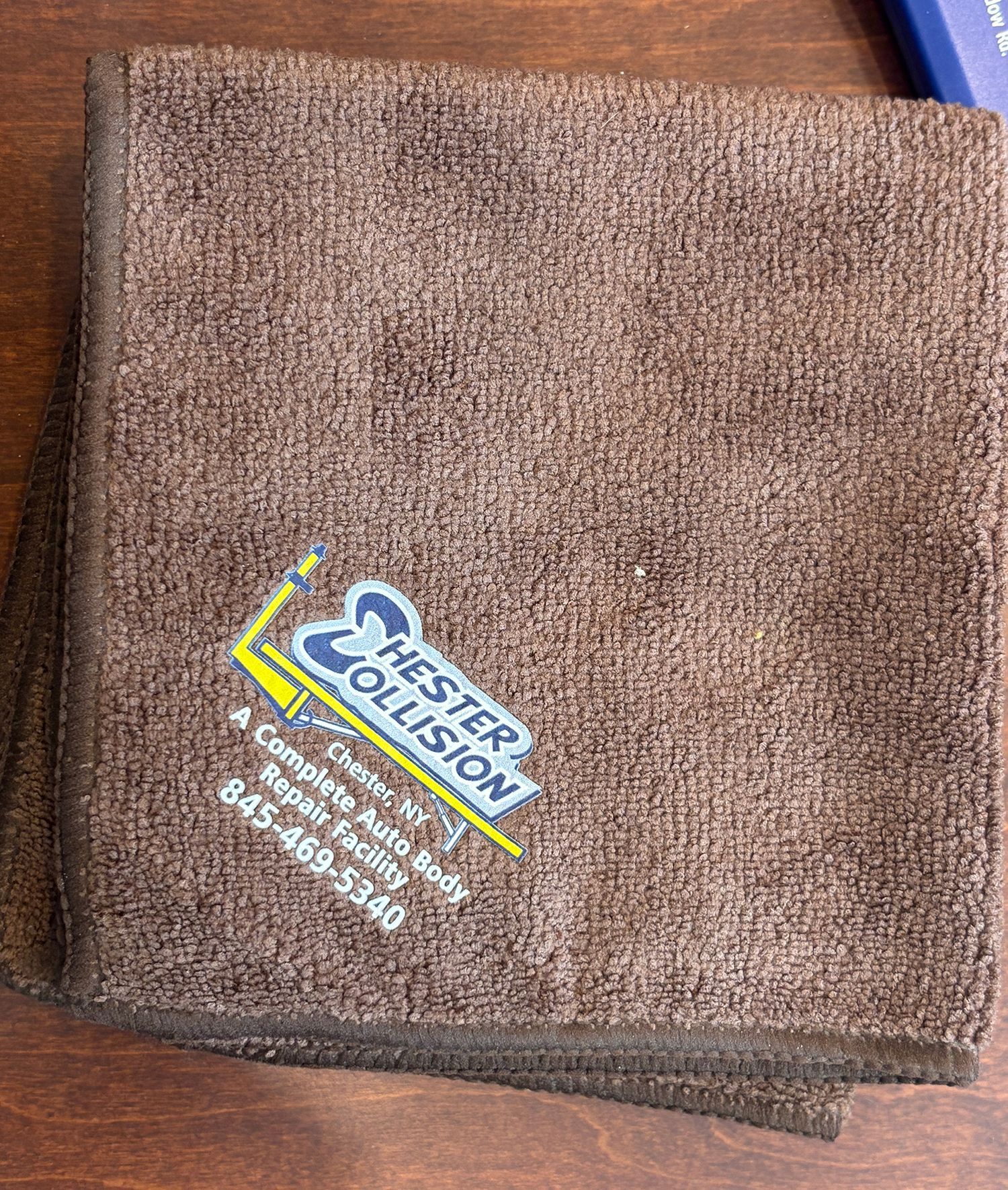 Brown folded towel with Chester Collision Inc's logo