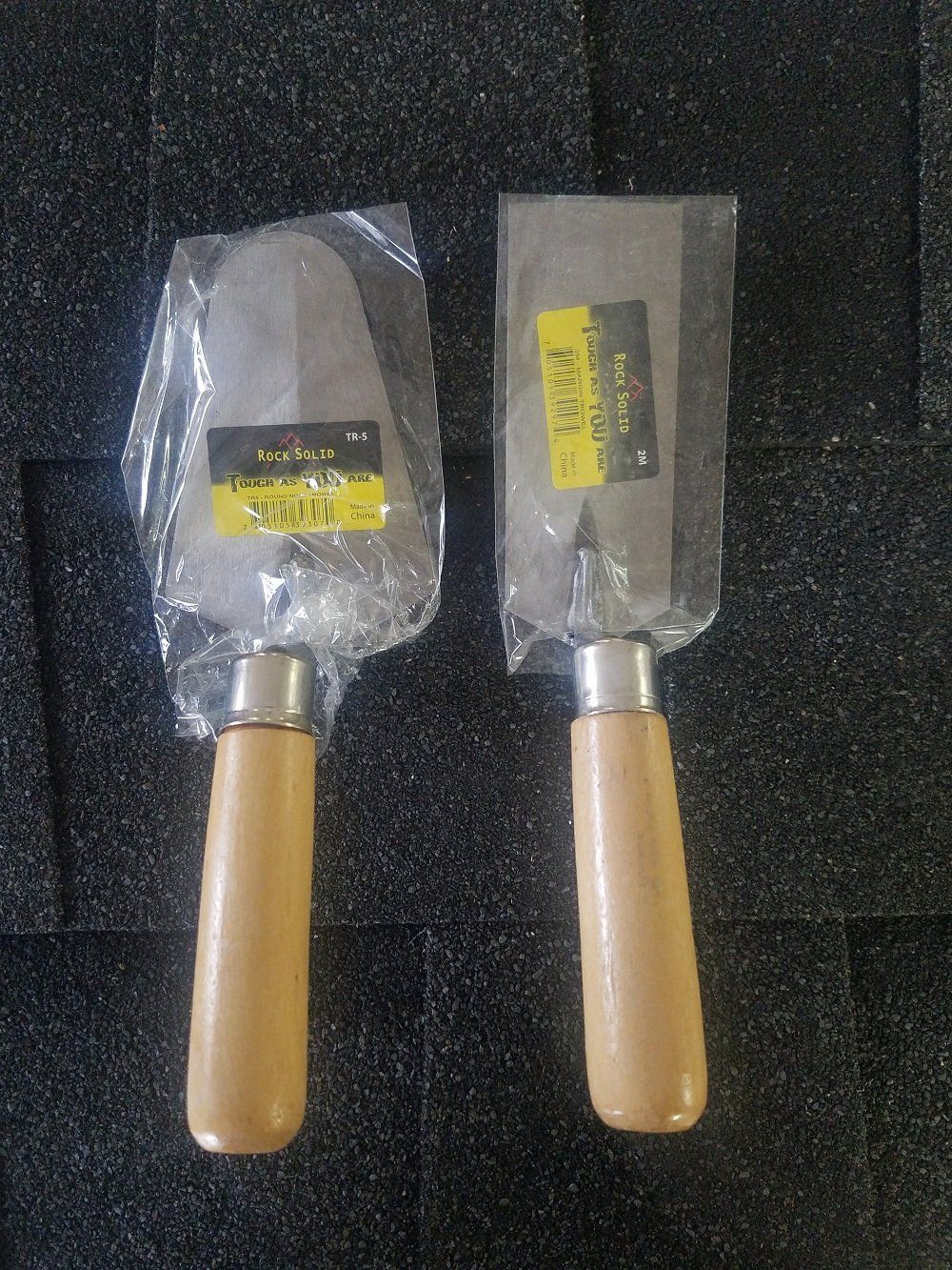 Two new trowels with wooden handles in plastic wrapping.