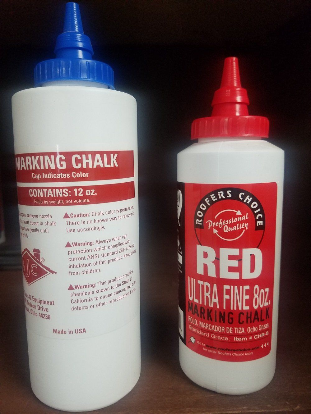 Two white bottles of marking chalk, one with a blue top, the other red, against a dark background.