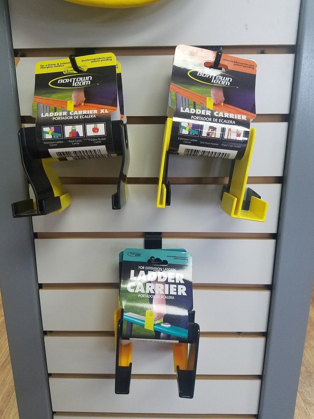 Three ladder carriers in yellow and black packaging, displayed on a slat wall.