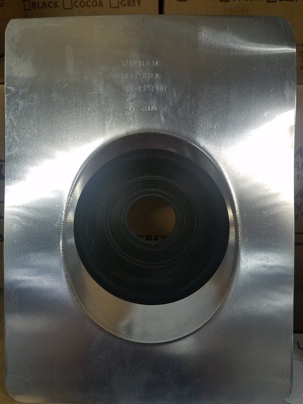 Metal roof flashing with a circular opening, likely for a pipe, against a neutral background.
