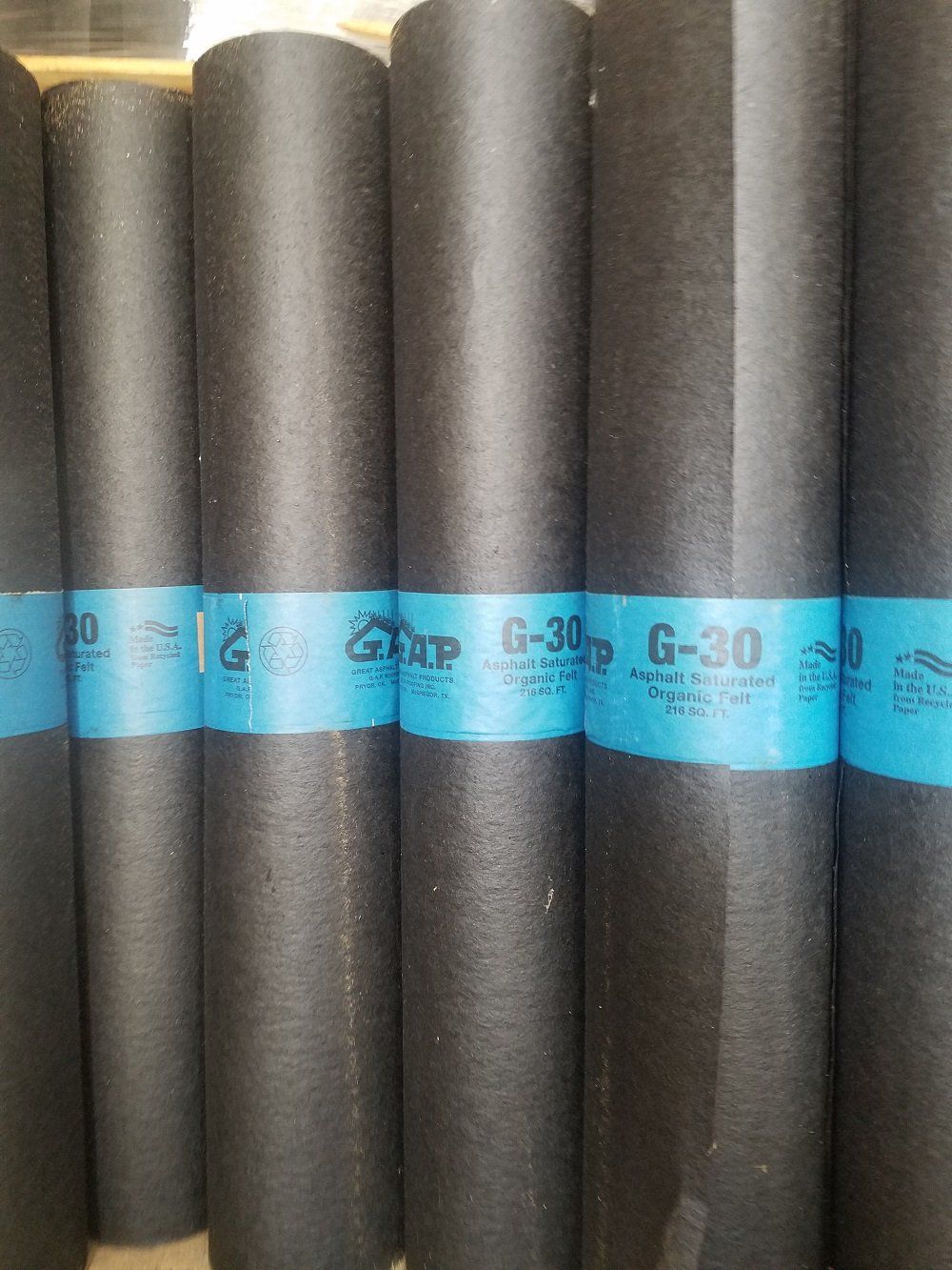 Black rolls of G-30 roofing underlayment with blue labels.