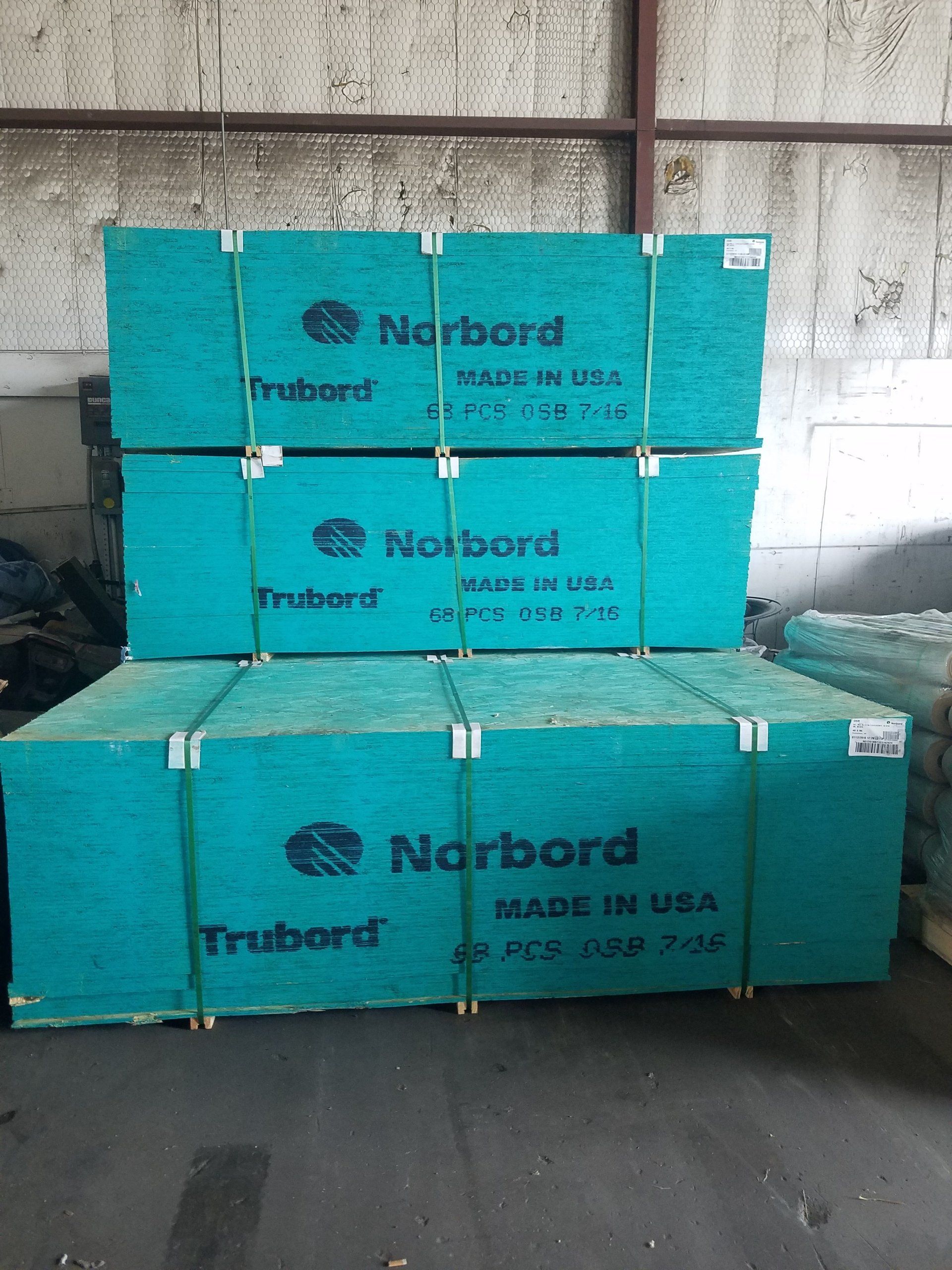 Three stacks of green Norbord wood panels, made in USA, banded together indoors.