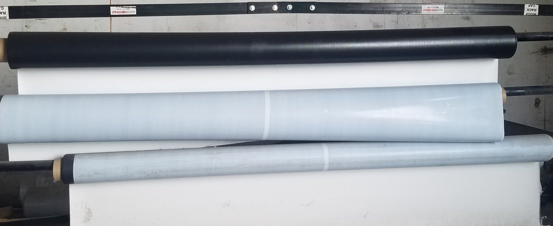 Three rolled sheets of material in black, white, and blue.